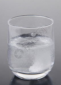 灰色背景下一杯水中的泡腾片图片