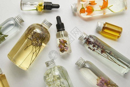 带有天然美容产品和灰底干枯野花的透明瓶子顶部视图以背景图片