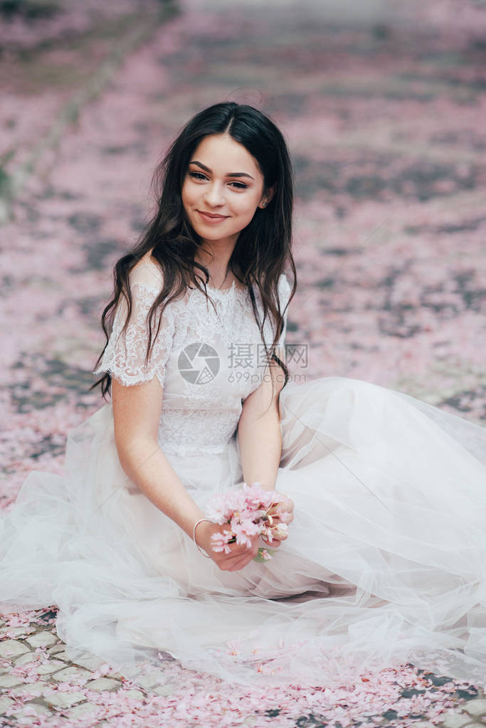 一个穿着白色婚纱的美丽女孩坐在花瓣中图片