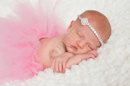 睡着8天大的新生女婴穿着粉红色的芭蕾舞短裙和水钻头带她趴着睡在一条白色背景