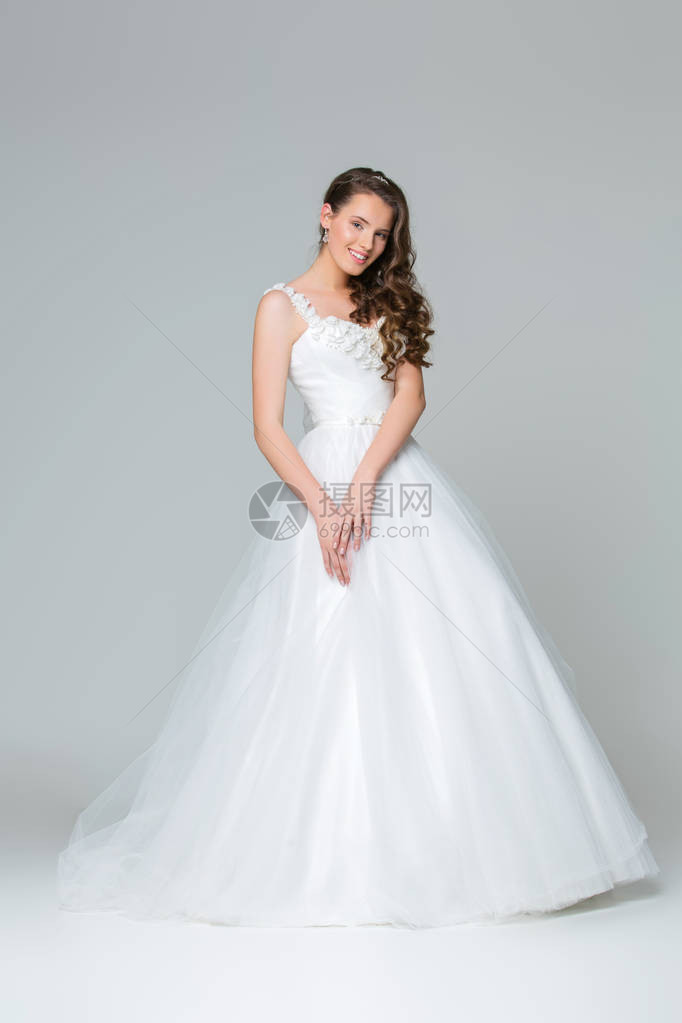 穿着长白色婚纱的美丽年轻新娘工作室拍的是灰色背图片