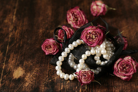 木质背景上带干粉红玫瑰的复古珍珠背景图片