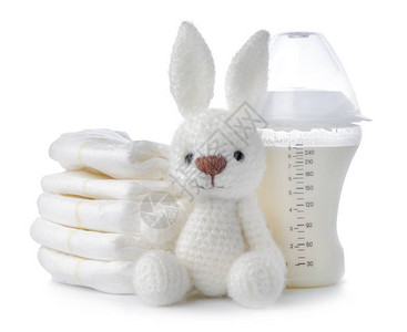 白色背景中带牛奶尿布和玩具兔子的奶瓶图片