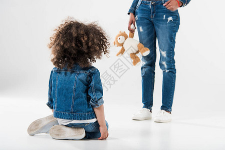 带着玩具站在坐地板上的女儿面前的美国母亲面前图片