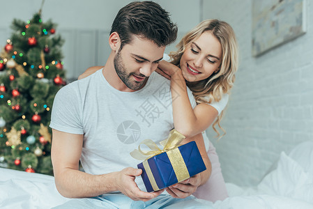 美丽的年轻美女向在家床上的男朋友提供圣诞节礼物图片