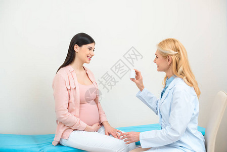 向年轻孕妇展示一罐药丸的妇背景图片