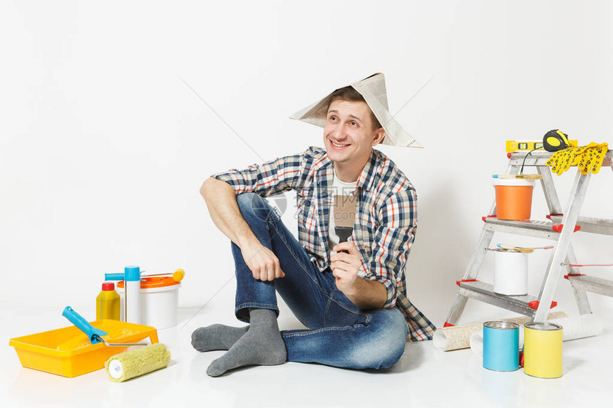 快乐微笑的年轻人在报纸帽子与腻子刀工具翻新公寓房间隔离在白色背景图片