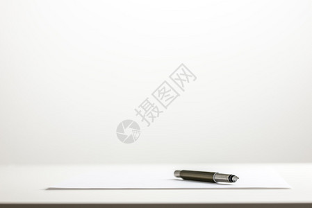 白色桌面上的一张空白纸上的一支笔的低角度视图图片