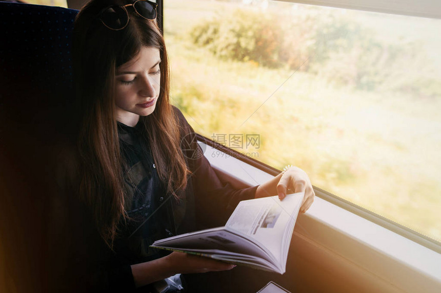 时尚的时髦女孩在火车的窗户灯看书乘火车旅行的概念美丽的年轻女子拿着纸质书旅行和交图片