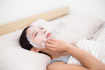 亚洲青年妇女在家里床上做纸面罩和阴梁的图片