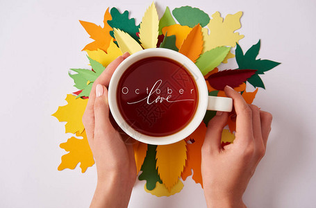 女在彩色纸做的叶子上部分地拿着热茶和八十图片