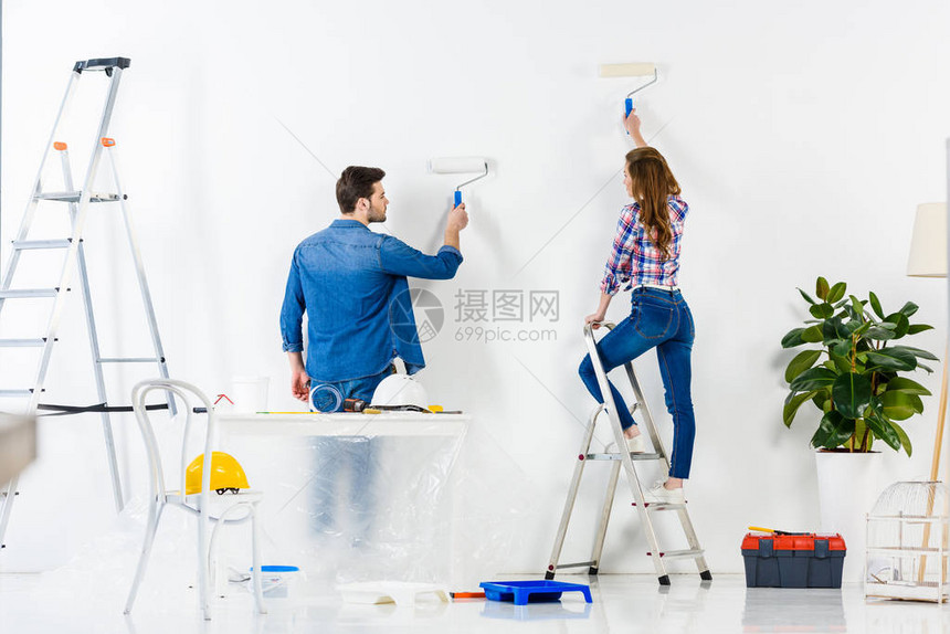 夫妇用白色油漆画墙的后视图图片