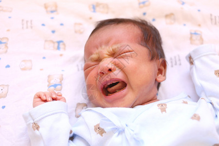 新生的Asia婴儿在白床上哭泣看着一图片