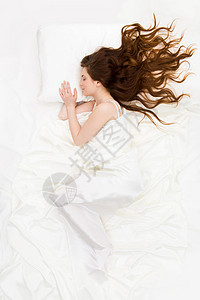 白色缎布床单下熟睡女人的上方视图图片