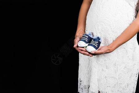 孕妇穿着衣服站在肚子前拿着一双小鞋子图片