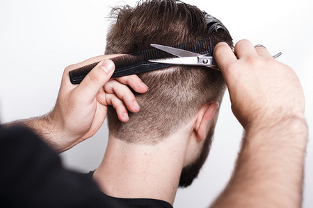 理发师用黑色梳子和剪刀为留着胡子的男人做新发型图片