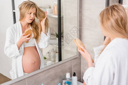 怀着毛发问题的不快乐孕妇站在浴室镜子图片