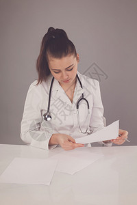 身穿白袍和颈部有听诊器的护士正在用灰色背景在白图片