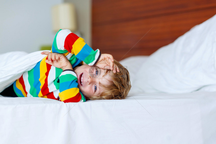 可爱的小男孩穿着五颜六色的睡衣在他的白色床上有趣的快乐孩子玩耍和微笑家庭假图片