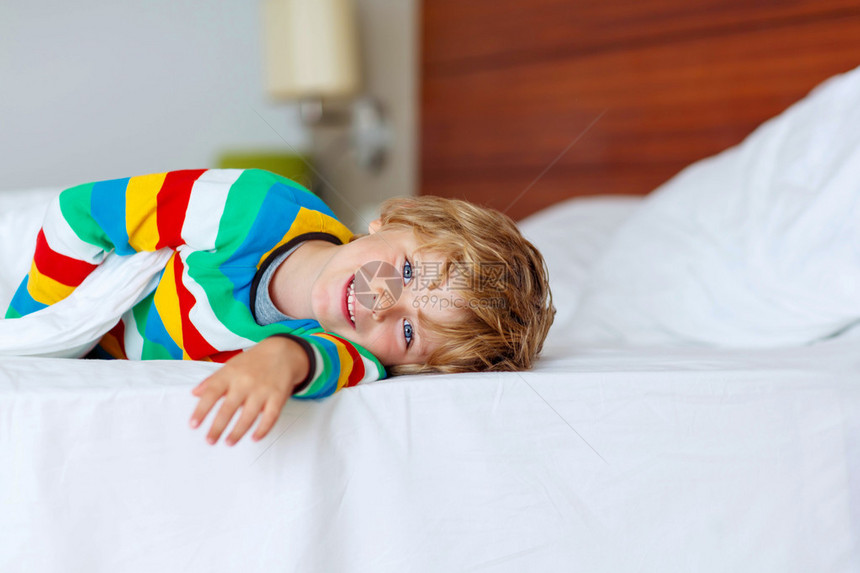 金发小男孩穿着五颜六色的睡衣在他的白色床上有趣的快乐孩子玩耍和微笑家庭假图片