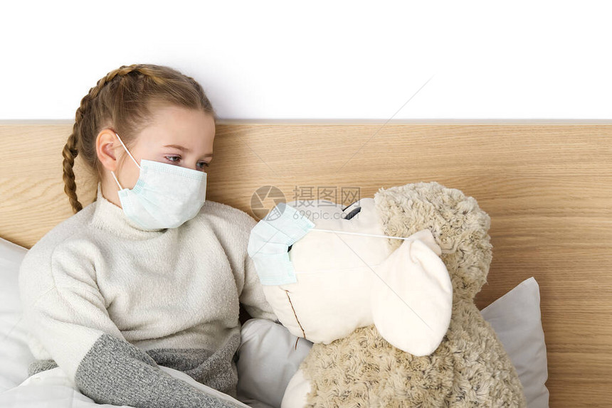 一个带着温度和的面具的生病悲伤的孩子躺在床上流感冒细菌在卧室里带玩具的女孩戴上防护面具图片