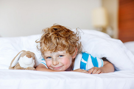 和玩具睡在白床上的可爱男孩小快乐的孩子跟玩具兔图片