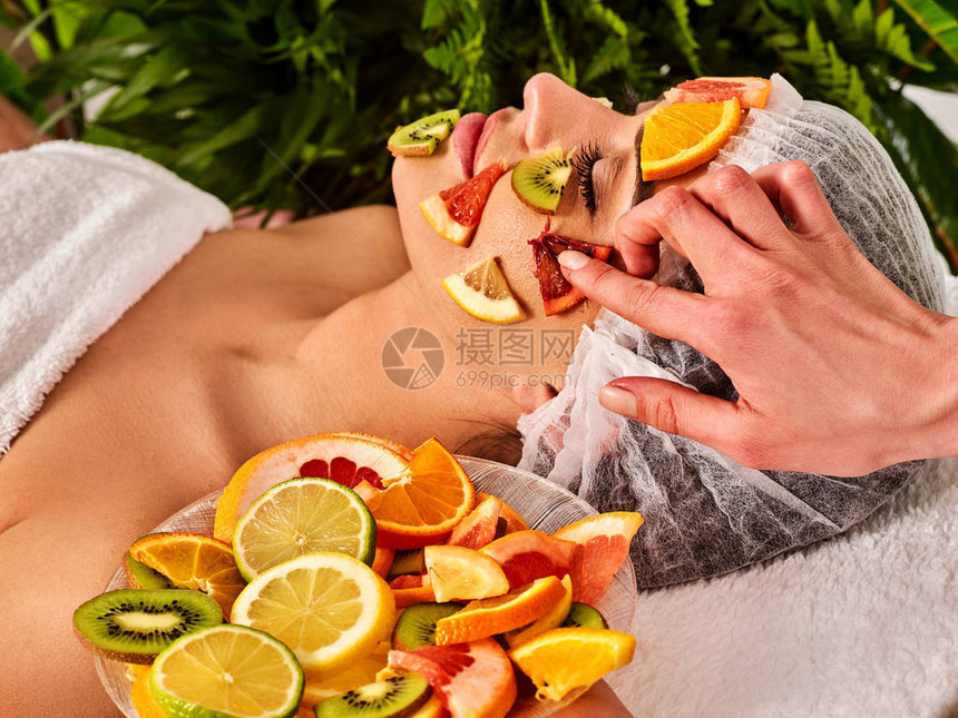 女用新鲜水果制成的面膜美容师涂抹芒果肉葡萄柚和猕猴桃戴着医疗帽的女孩躺在水疗床上参观水疗沙图片