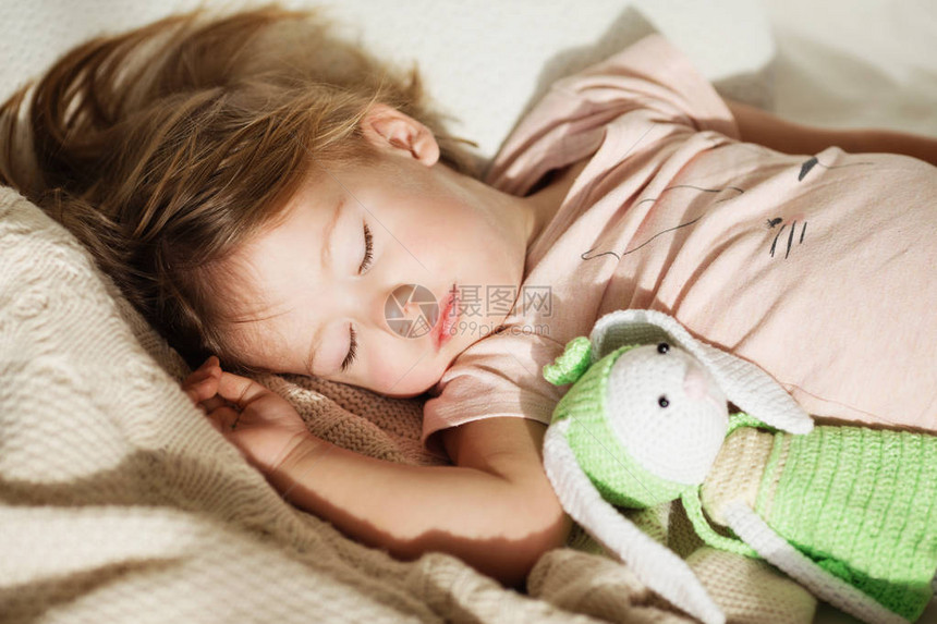 睡着的小女孩无忧虑地睡在床上的毛绒玩具的小宝一个漂亮的熟睡儿童在针织毯子上的特写肖图片