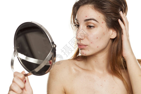 皮肤有问题没有化妆的年轻女子在白色背景的镜子里照着自己的面图片