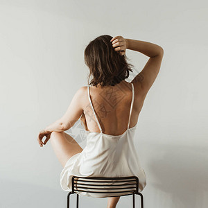 穿着丝绸内衣的年轻美女坐在白色背景的黑凳子图片