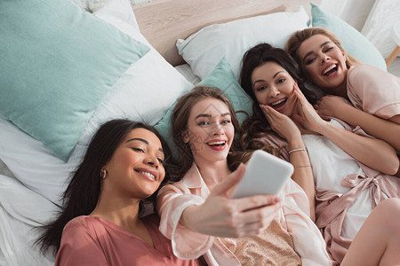 兴奋的多文化女在单身派对上睡觉时自拍的高角度视角图片
