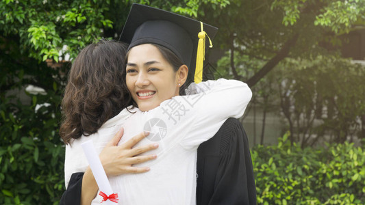 带着毕业礼服和帽子拥抱家长的女学生在图片