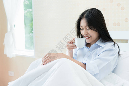 亚裔年轻女子在家卧室睡觉时喝咖啡图片