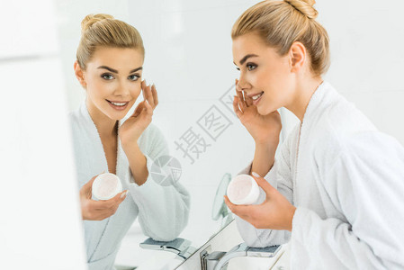 白浴袍中有吸引力的金发美女使用面霜和照镜子时有图片