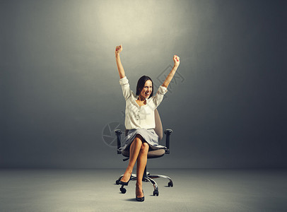 幸福的成功女人坐在椅子上举起手来图片