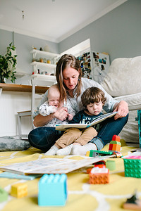 快乐的年轻母亲读书给坐在房子地板上的孩子看书图片