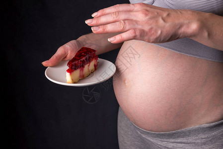 一个肚子里拿着一块芝士蛋糕的孕妇怀孕期间体重控制和不健图片