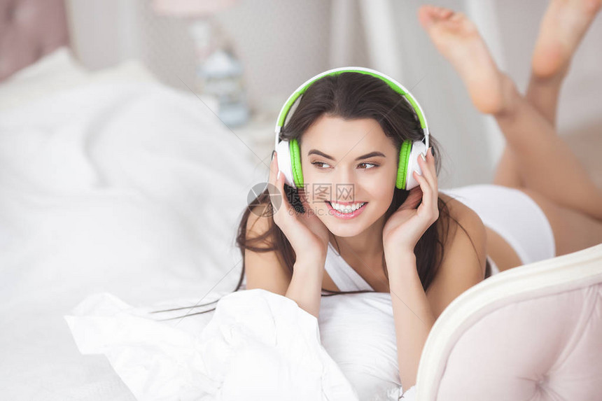 年轻有魅力的女人听音乐耳机的可爱的女孩女人在床上放松图片