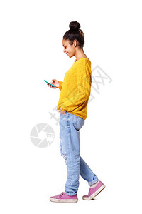 放松的年轻女子在白色背角上行走和手机短信的全身侧面肖像图片
