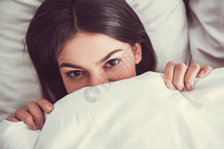 躺在床上的快乐女孩把脸藏在毯子下玩得图片