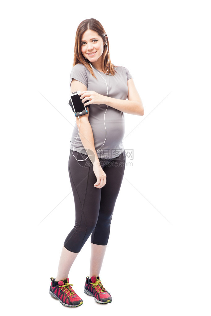 可爱的年轻孕妇在锻炼时用耳膜和智能手机听手带图片