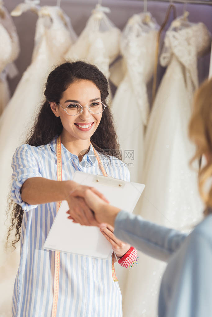 女裁缝和新娘在婚纱时装店握手图片