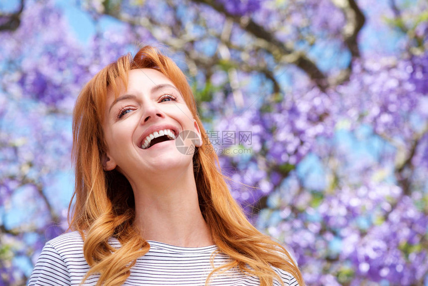 迷人的年轻女子用紫花笑在树边图片