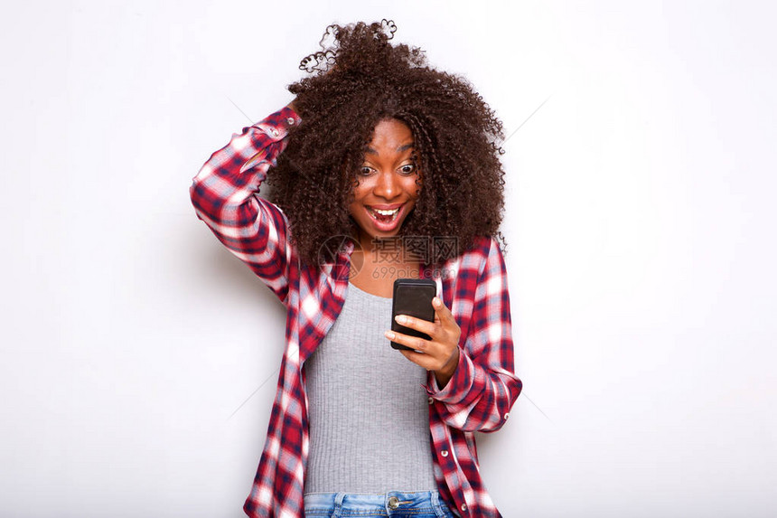 年轻非裔美国女在白色背景下惊讶地看待手机的肖像图片