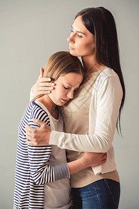 美丽的年轻妈拥抱着她的少女灰背景图片