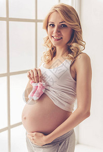 美丽的孕妇摸着肚子拿着鞋和微图片