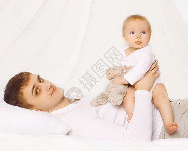 父亲和孩子在家躺在床上孩子们玩泰迪熊图片