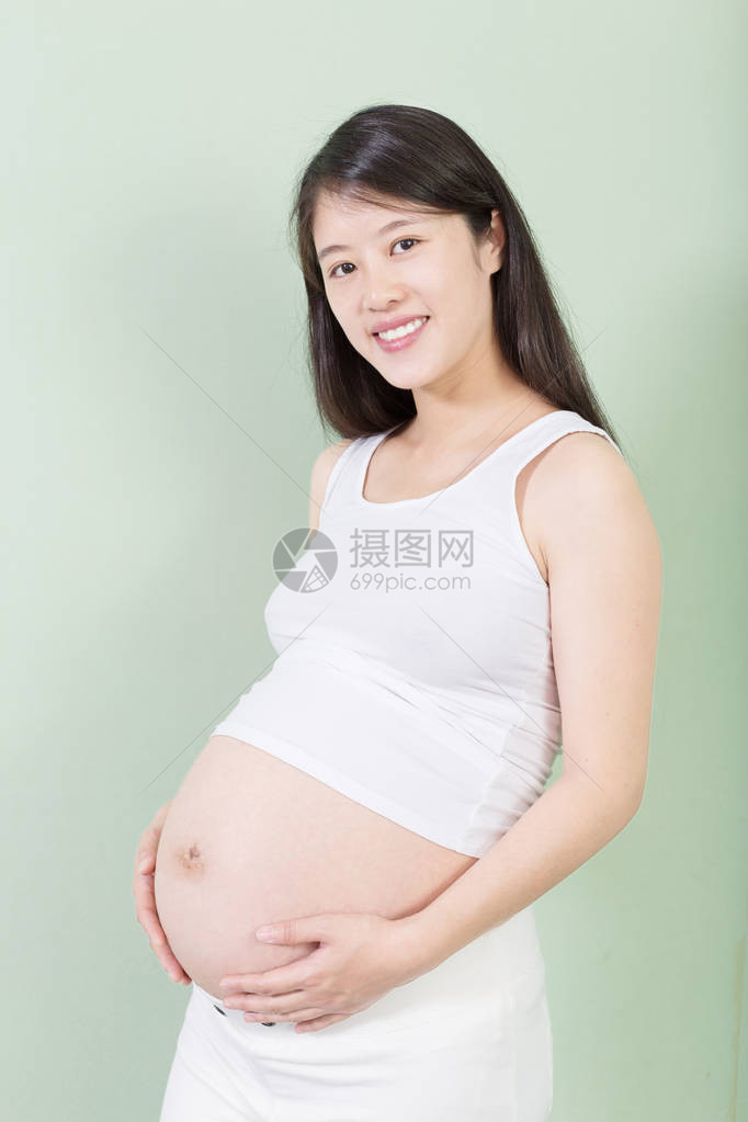 年轻漂亮的怀孕少女背着她的肚子在背景上图片