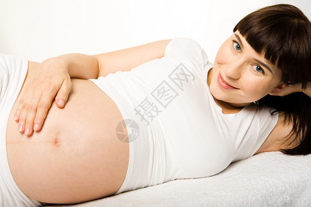 孕妇在触摸其肚子时躺着看照相机并看图片