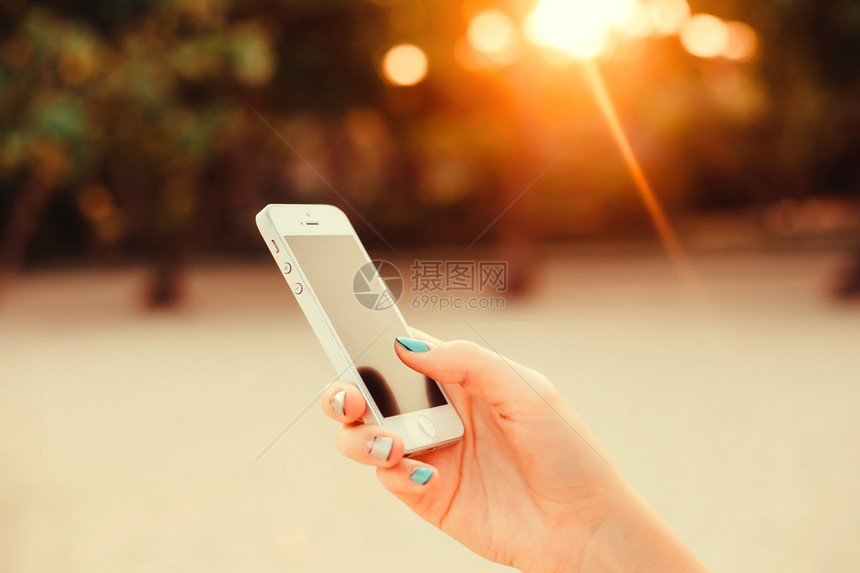 背景日落完美甲日光浴的女孩手持智能手机的特写图像黑屏手机短信视频通话海滨假期工作图片